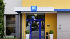 The entrance to ibis budget hotel with a blue door, two potted plants, and a sign above the door.