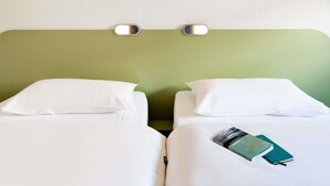 A hotel room with two beds, white bedding, a green headboard, and a wall-mounted light fixture.