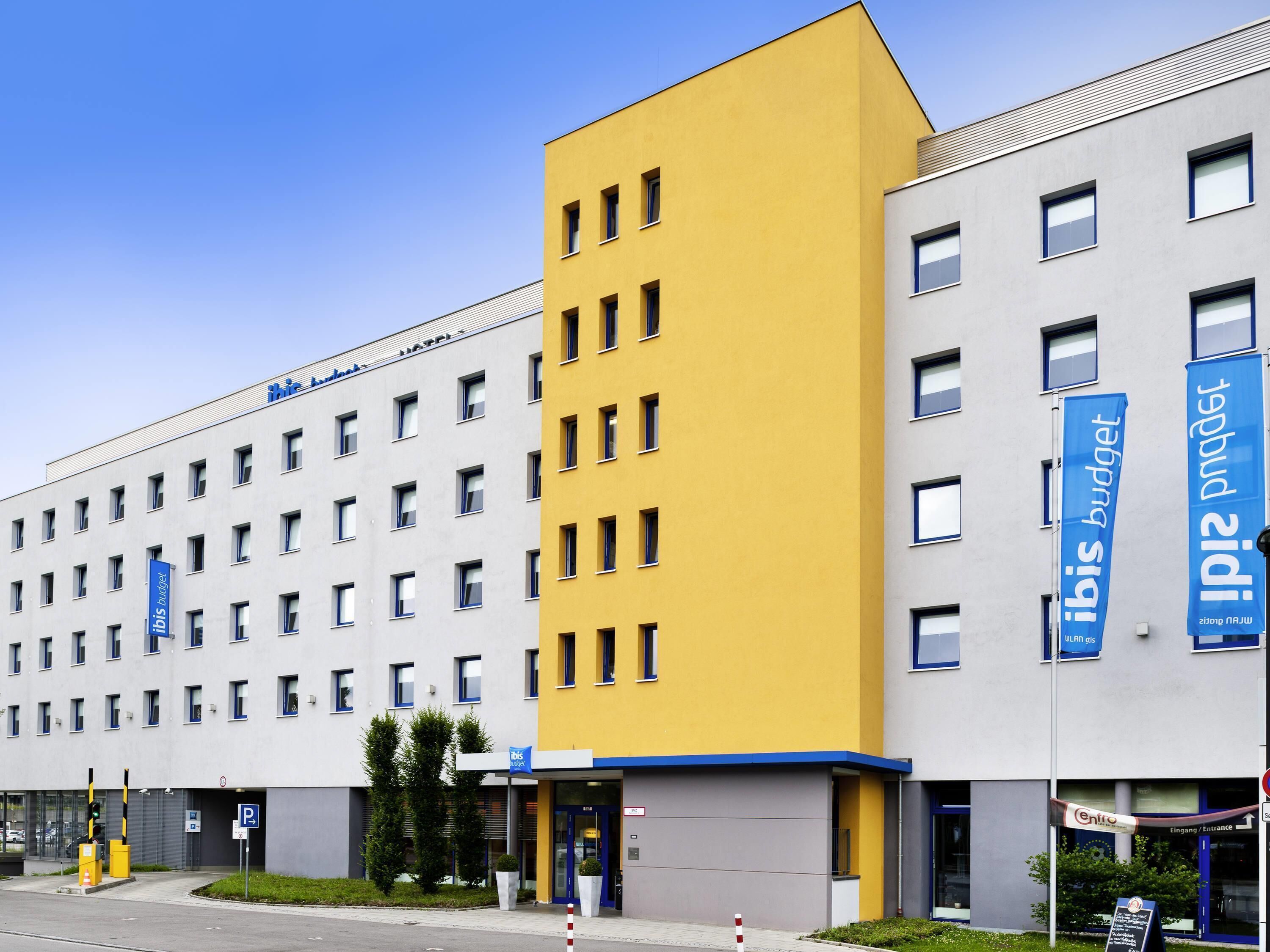 A modern hotel building with a yellow and grey facade, multiple windows, and a clear sky.