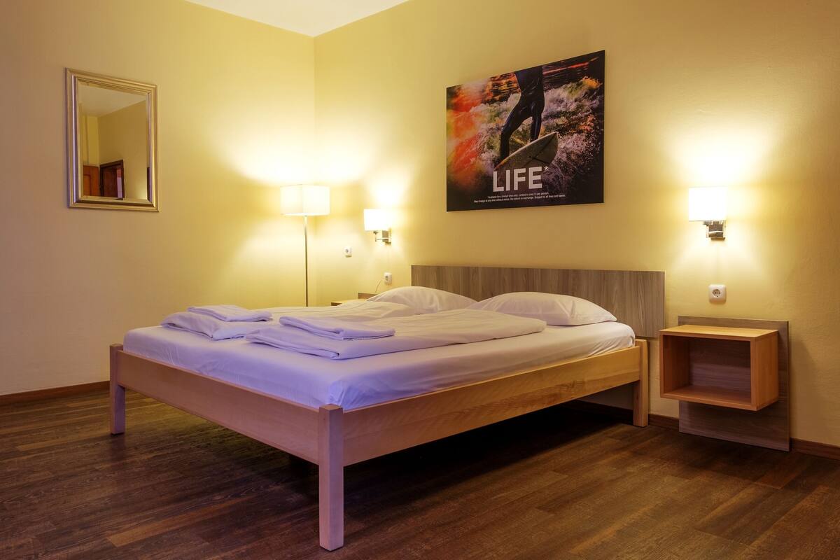 Un lit bien fait dans une chambre d’hôtel, avec une tête de lit en bois, deux tables de chevet avec des lampes et une affiche accrochée au mur.