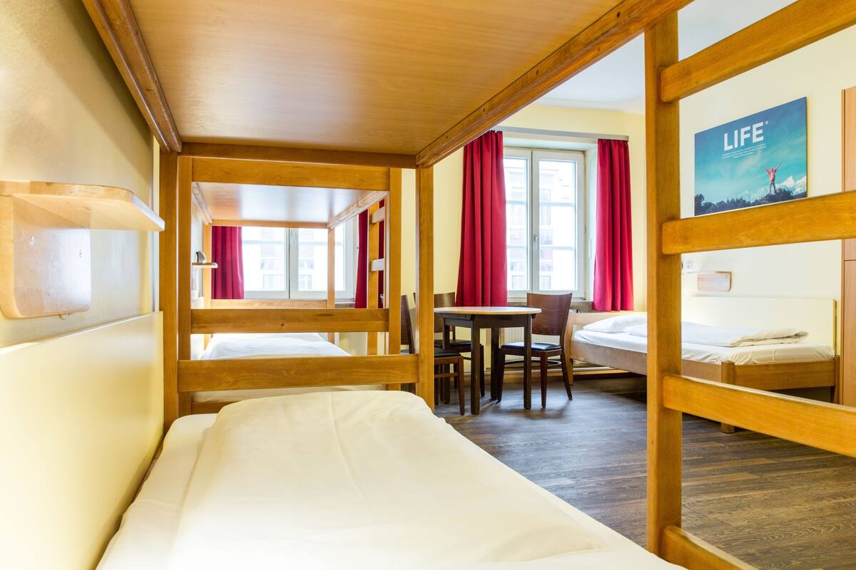 Une chambre avec un lit superposé, un bureau et une chaise. Il y a une fenêtre avec des rideaux et une affiche accrochée au mur.