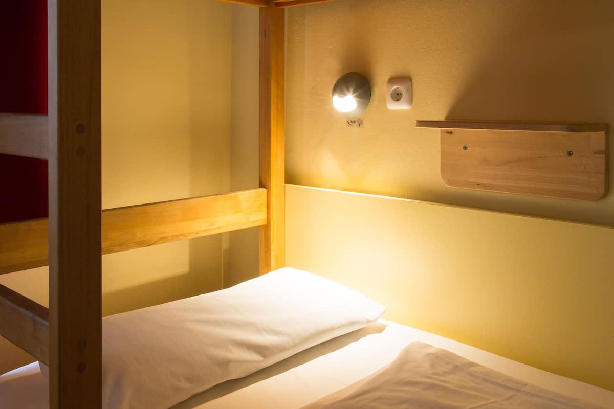 Un lit superposé avec une tête de lit en bois, une étagère fixée au mur et un luminaire fixé au mur.