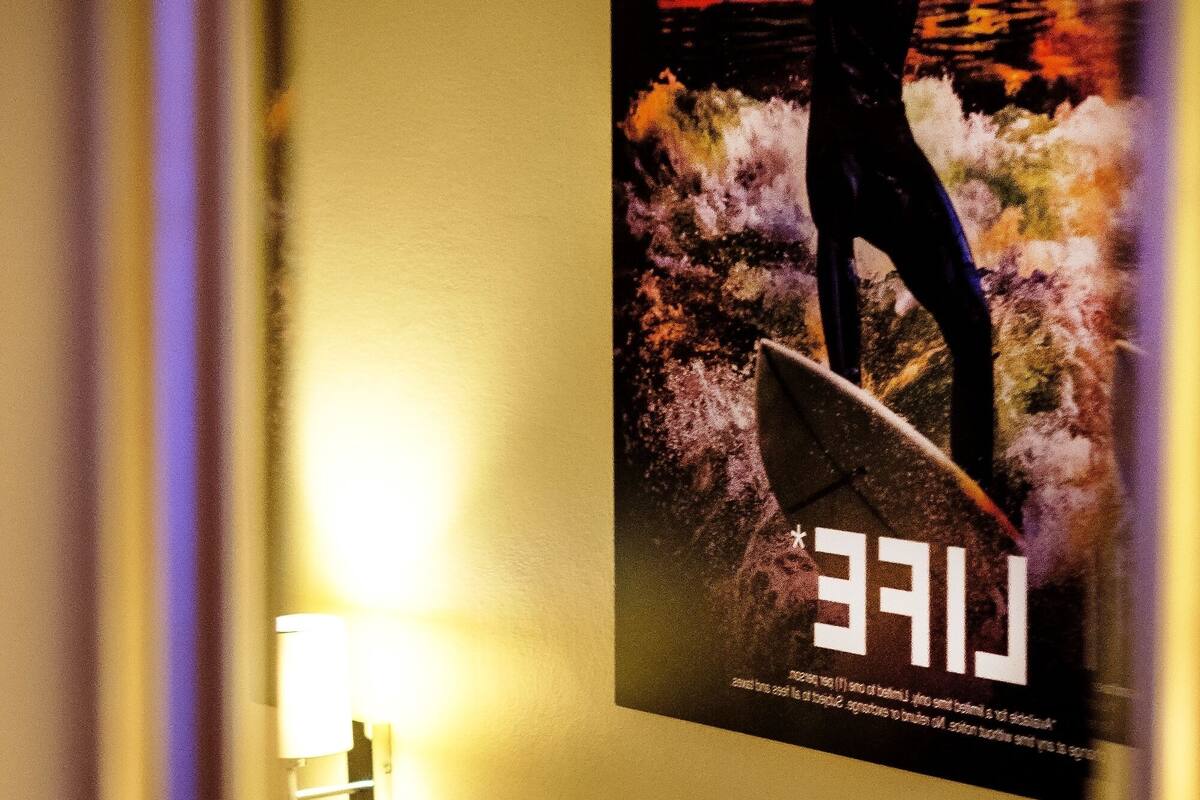 Une chambre d’hôtel avec un lit, une lampe fixée au mur et une affiche représentant un surfeur sur une vague.