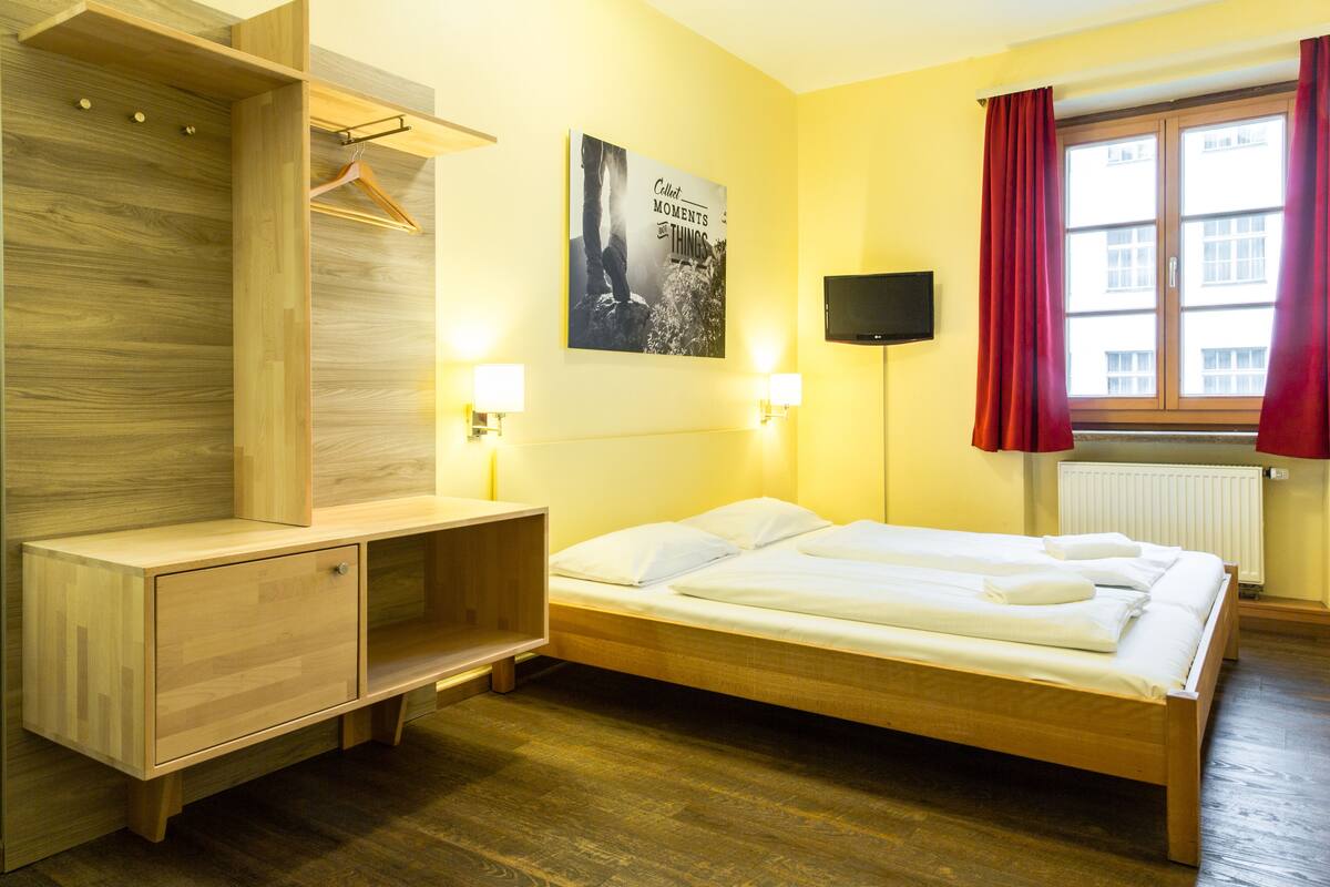 Une chambre à coucher avec un lit en bois, une armoire en bois, un téléviseur fixé au mur et une affiche accrochée au mur.