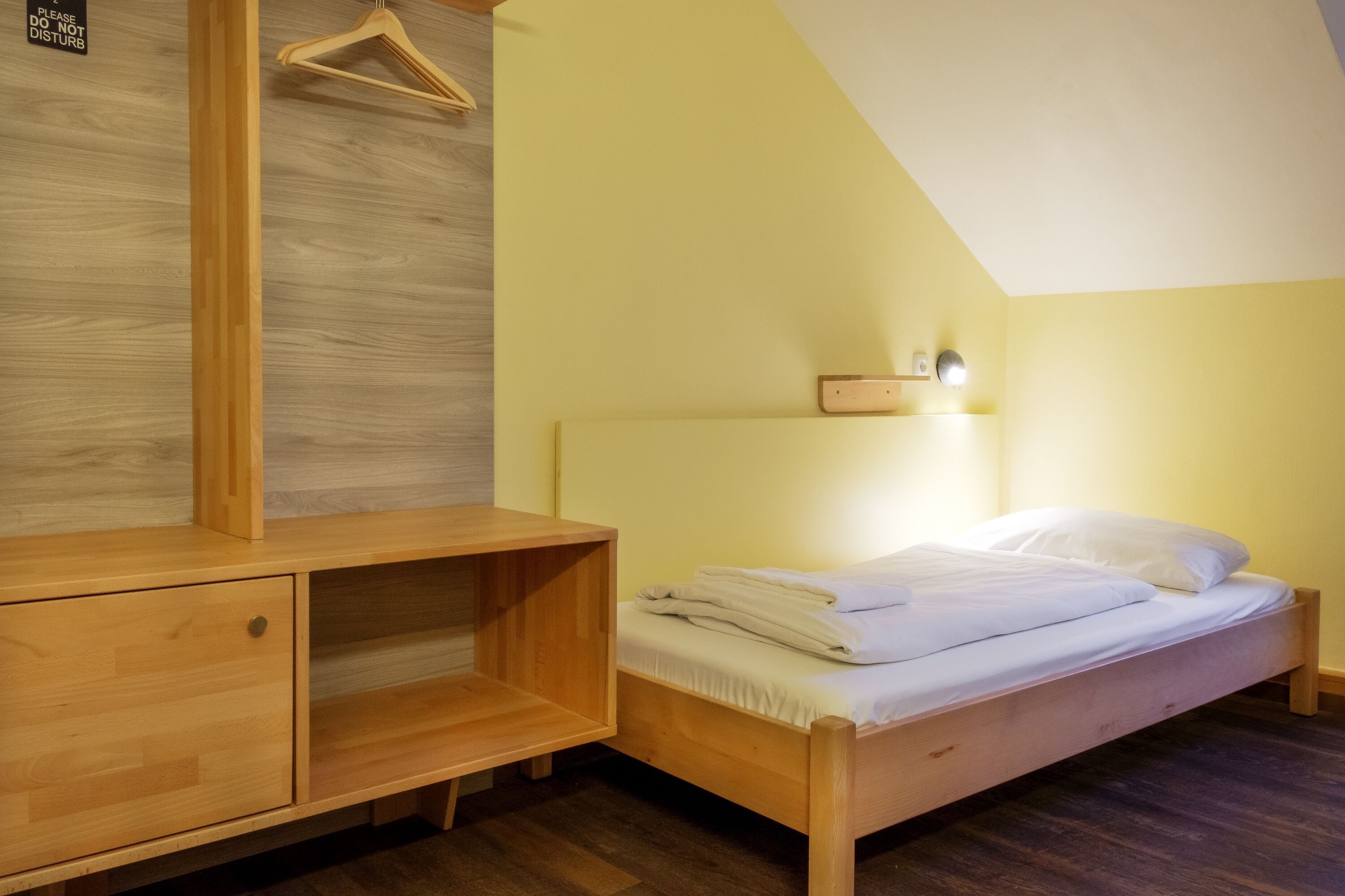 Ein Schlafzimmer mit einem hölzernen Bett, einem Nachttisch, einer Holzkommode und einem an der Wand montierten Regal.