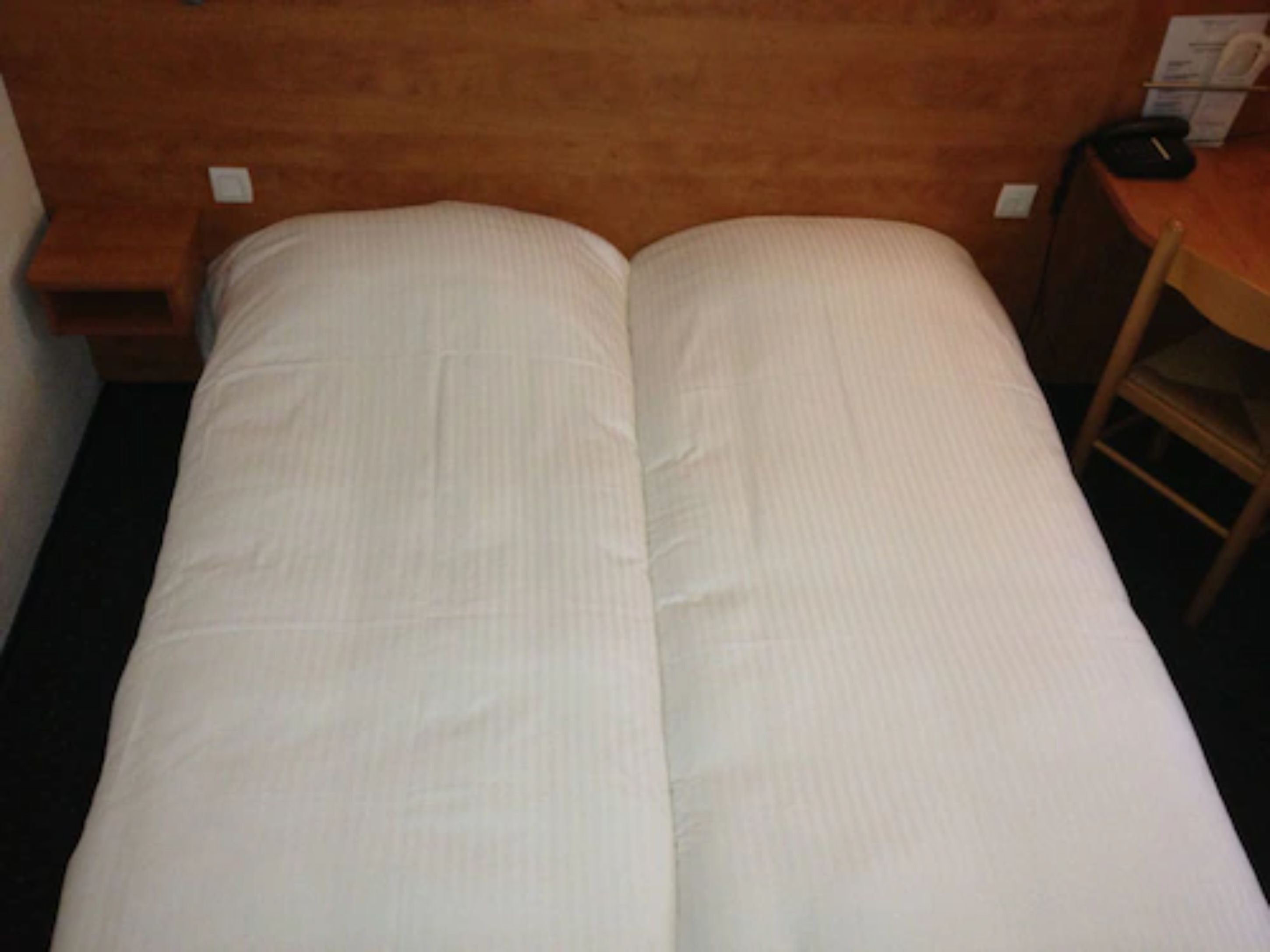 A standard hotel room with a single bed, a wooden headboard, a small wooden table, and a chair.