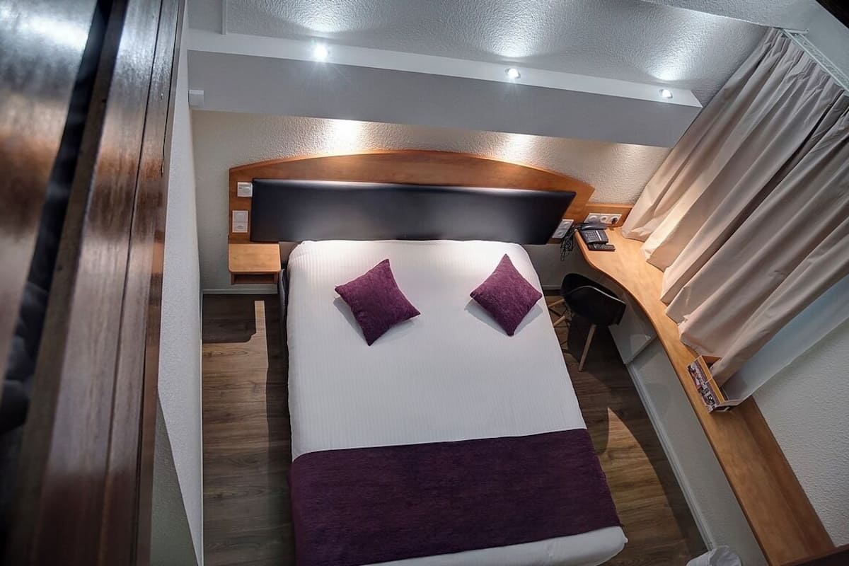Un dormitorio ordenado con cama, dos almohadas, una mesita de noche y cabecero.