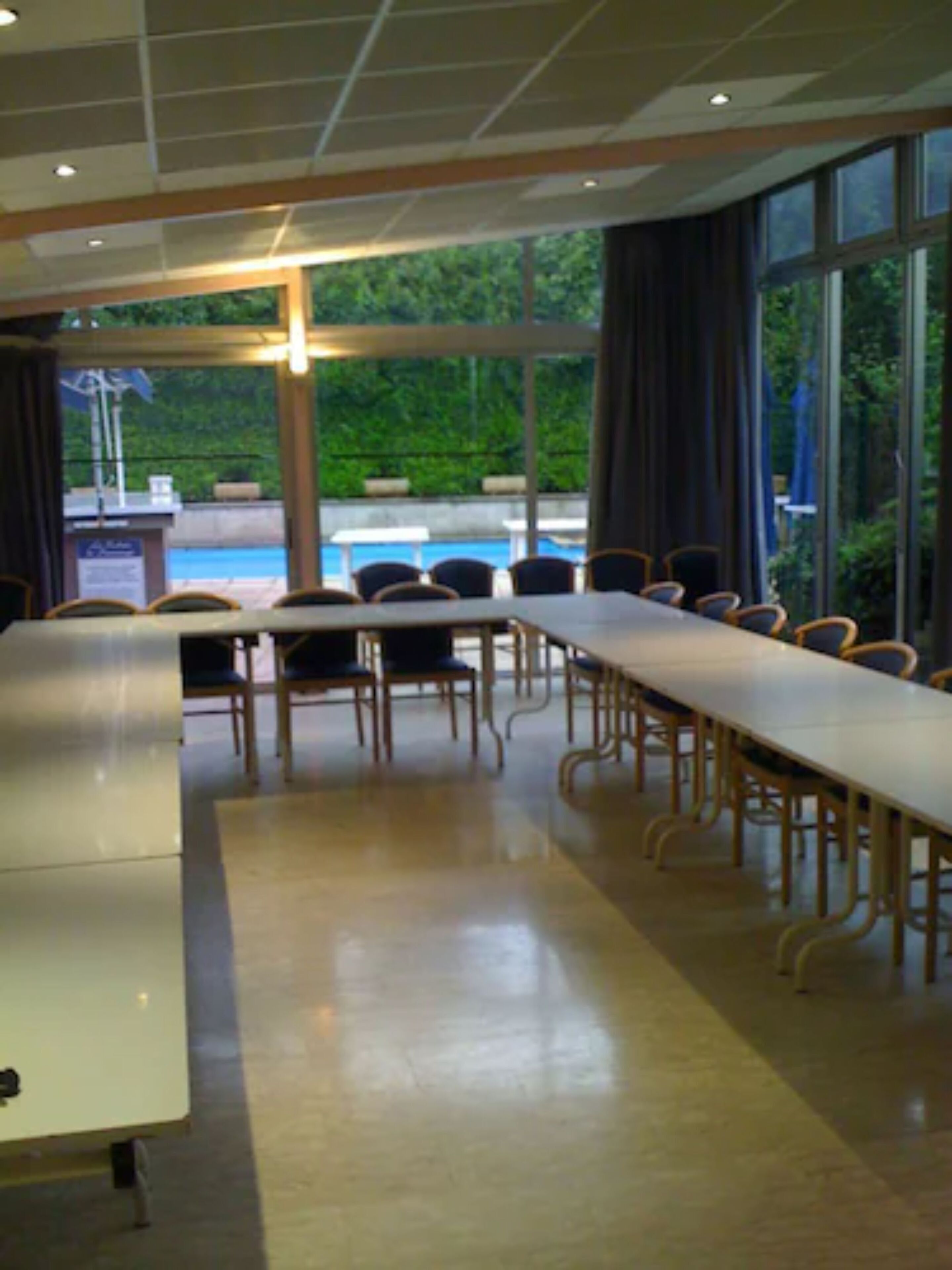 A conference room with a long table and chairs, large windows with curtains, and a view of a pool outside.