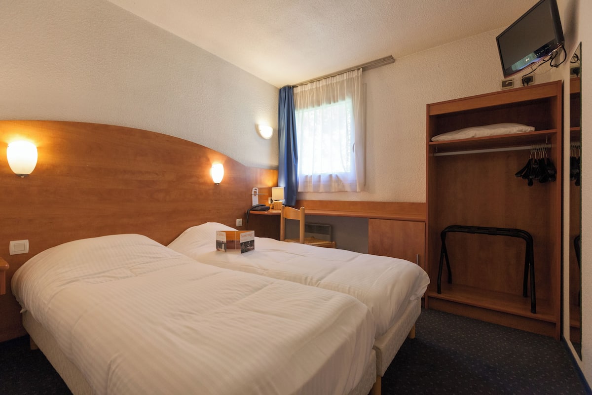 Habitación de hotel con dos camas, un escritorio, una silla, un televisor y un armario.