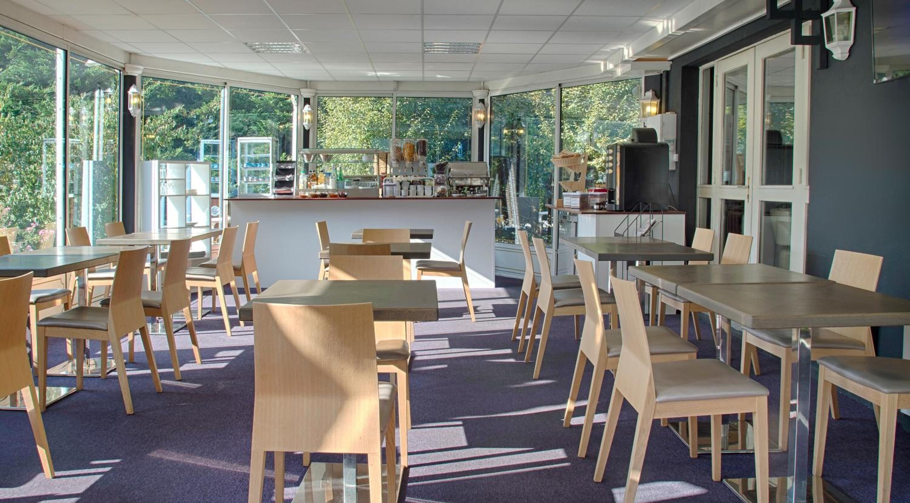Un restaurant offrant une vue sur la verdure, avec des tables et des chaises en bois, et un espace bar.