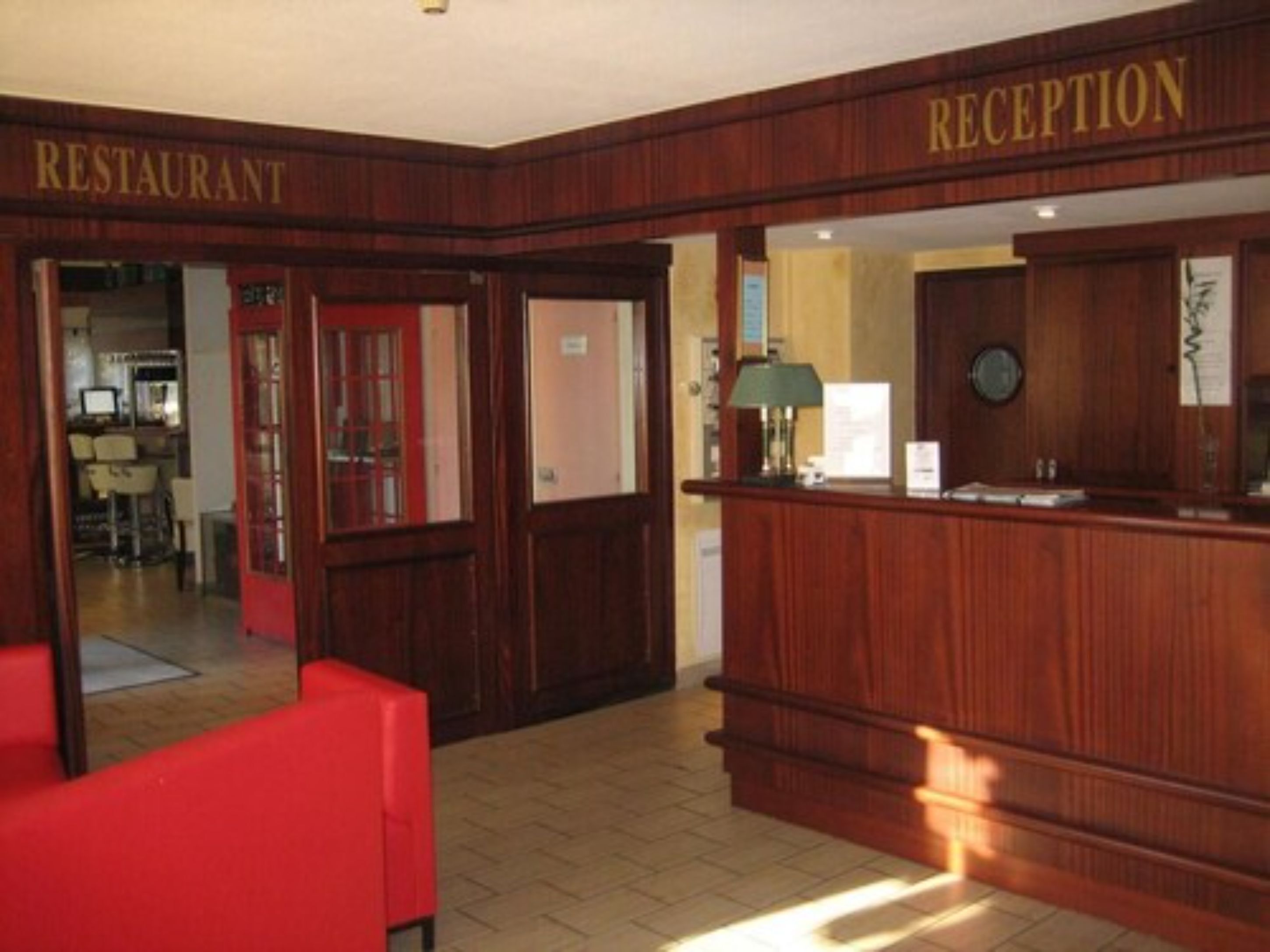 Un área de recepción con un mostrador de madera, una silla roja y un letrero que indica la entrada al restaurante.