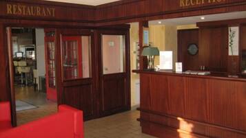 Un área de recepción con un mostrador de madera, una silla roja y un letrero que indica la entrada al restaurante.
