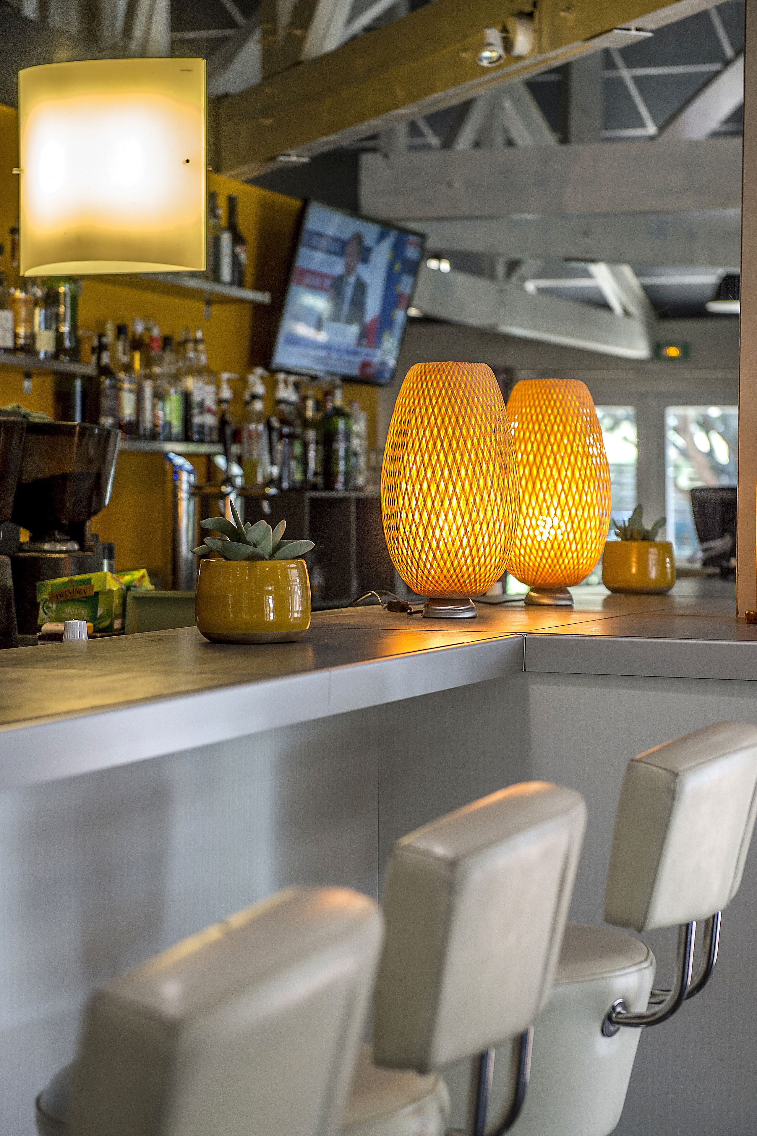 Un área de bar con dos lámparas iluminadas, una planta en maceta y una pantalla de televisión al fondo.