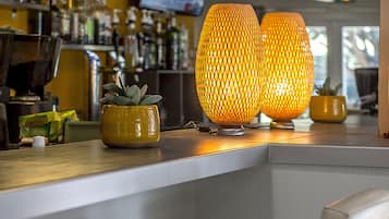 Un área de bar con dos lámparas iluminadas, una planta en maceta y una pantalla de televisión al fondo.