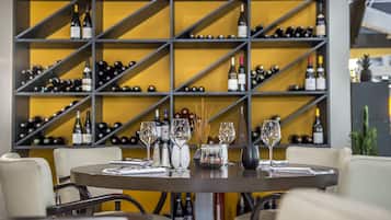A restaurant with a round table set for dining, a wine rack in the background, and a yellow wall.