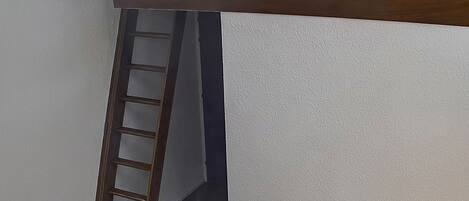 Un dormitorio con una cama, una manta púrpura y una escalera de madera apoyada en la pared.