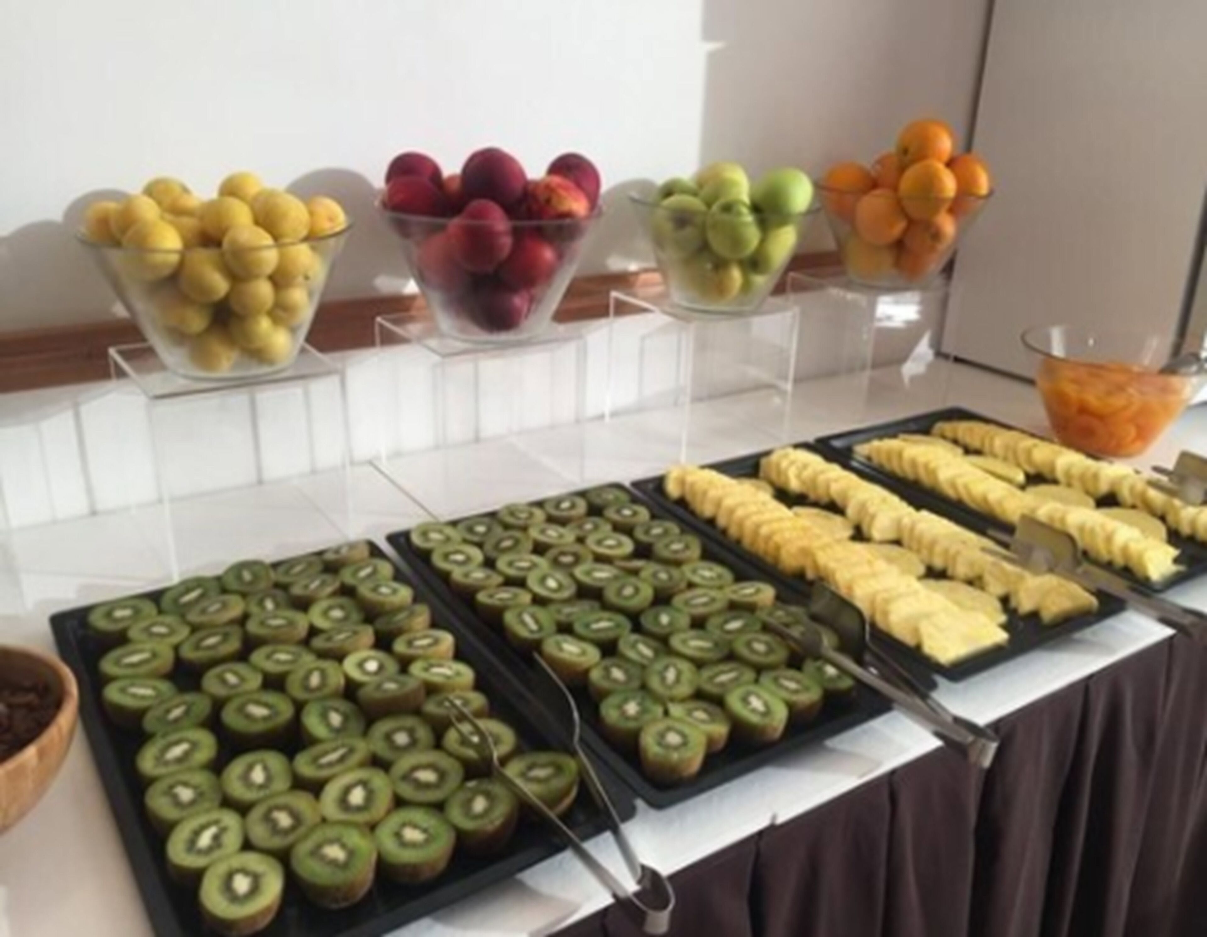 Un bufé con diversas frutas y plátanos en rodajas dispuestas en bandejas.