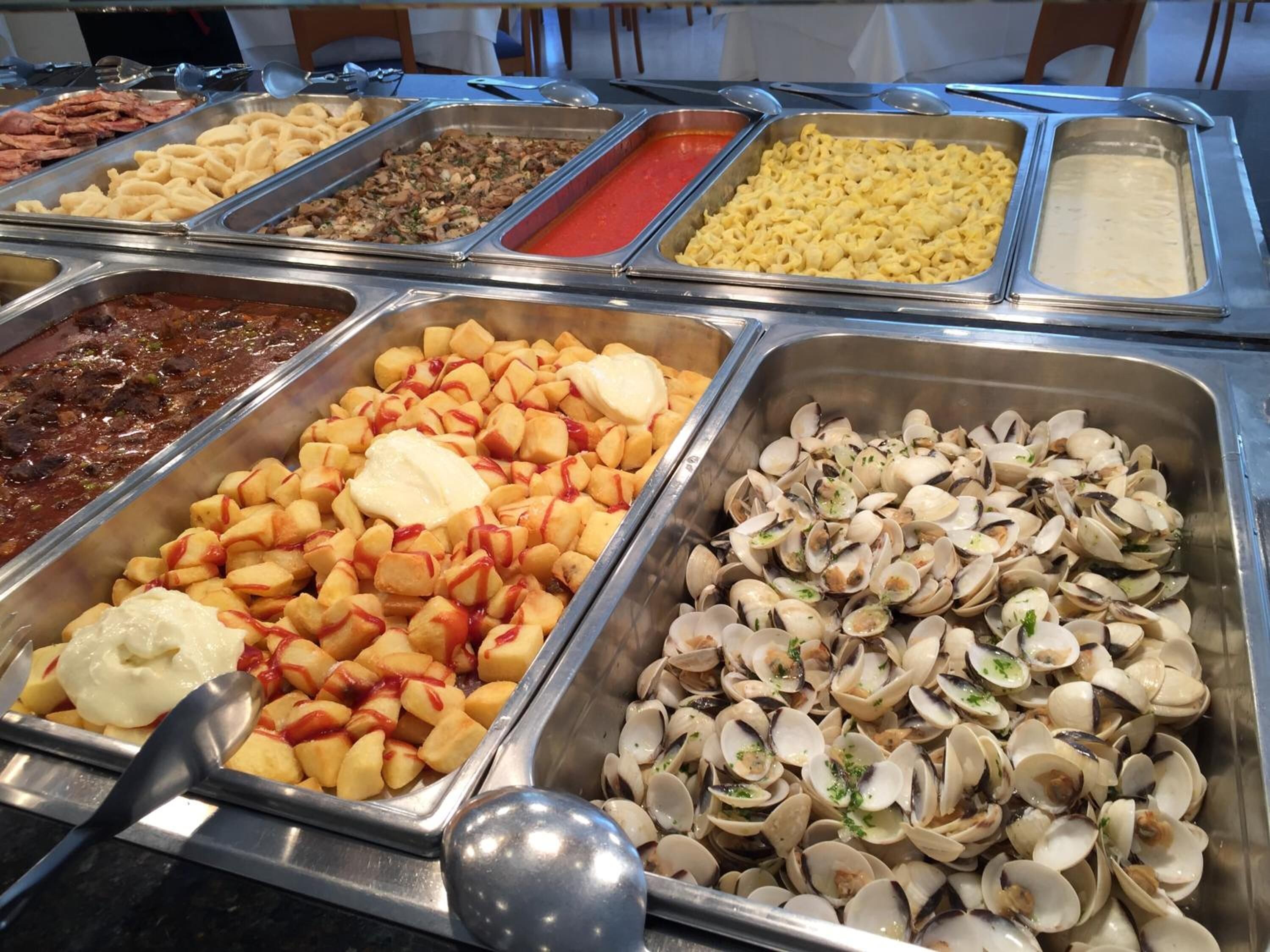A buffet with various food options including pasta, potatoes, and clams.