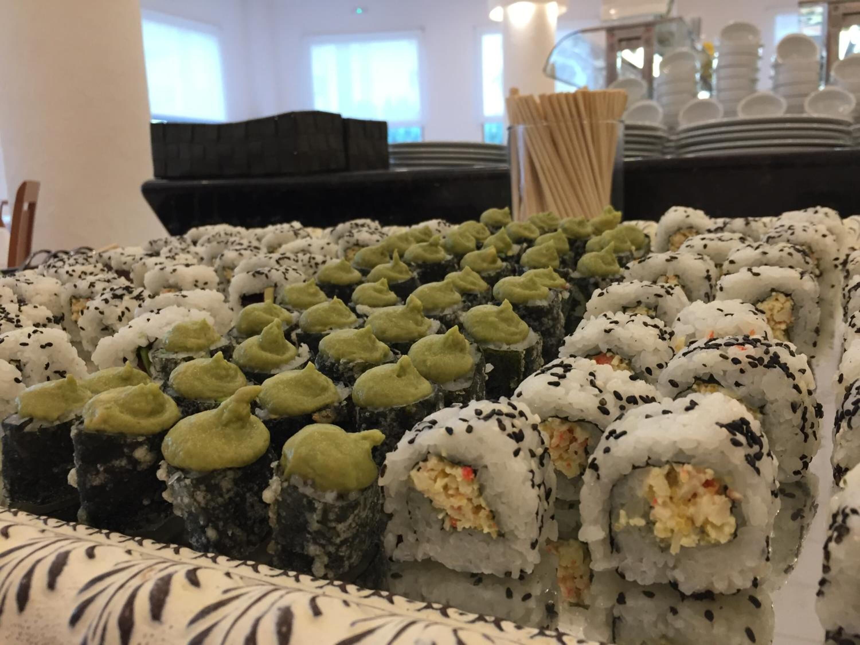 A sushi display with various types of sushi rolls, including some with green toppings and others with sesame seeds.