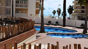 Ein Poolbereich mit Holzterrasse, Liegestühlen und Blick auf das Meer.