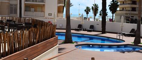 A pool area with wooden deck, lounge chairs, and a view of the sea.