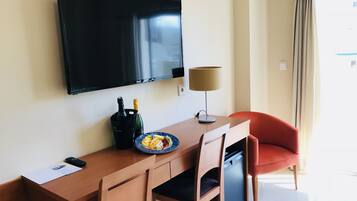 Een hotelkamer met een houten bureau, een aan de muur bevestigde televisie, een lamp en een rode stoel.