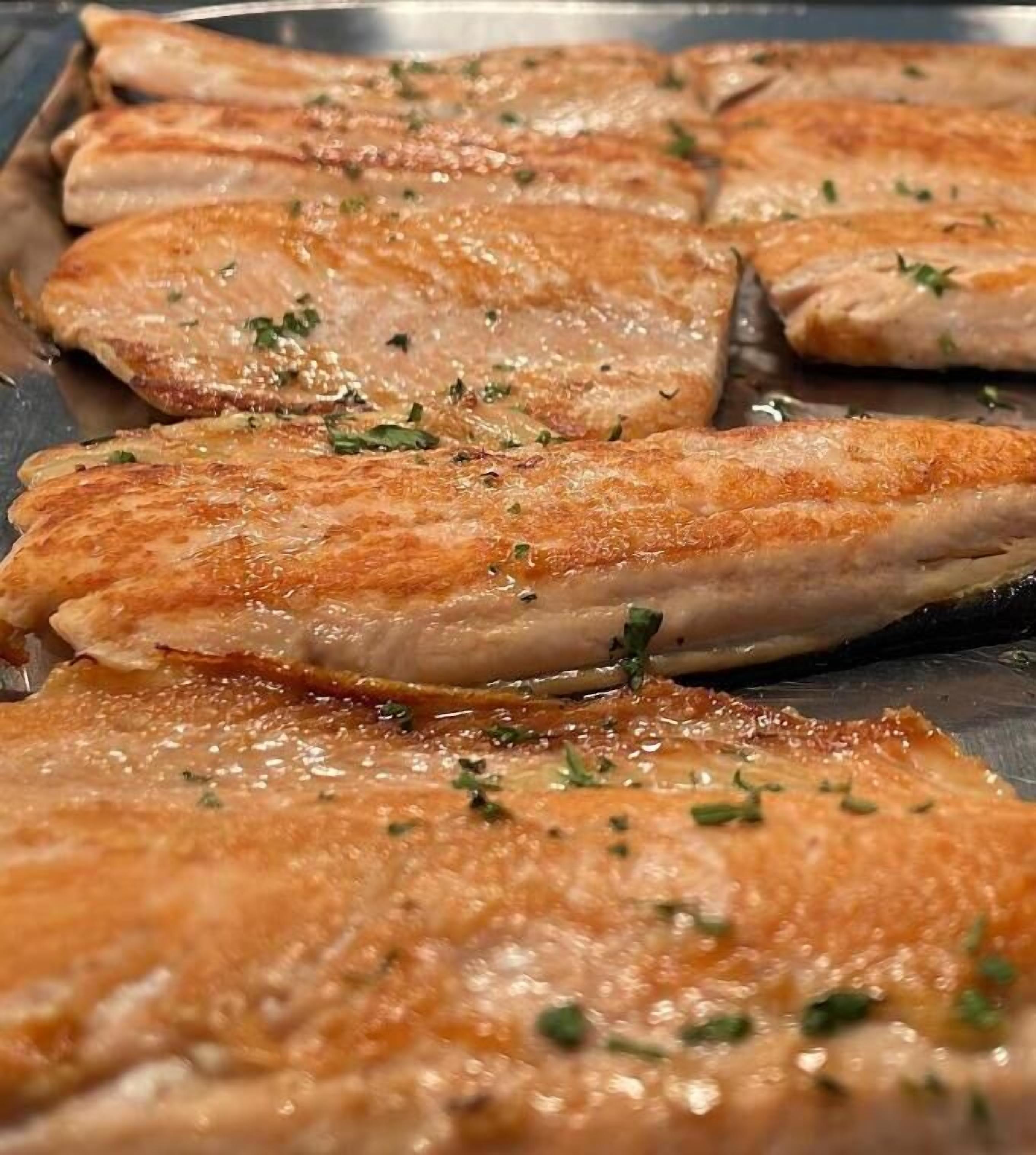 Gros plan sur des filets de poisson cuits, dotés d’une croûte dorée et parsemés d’herbes aromatiques.