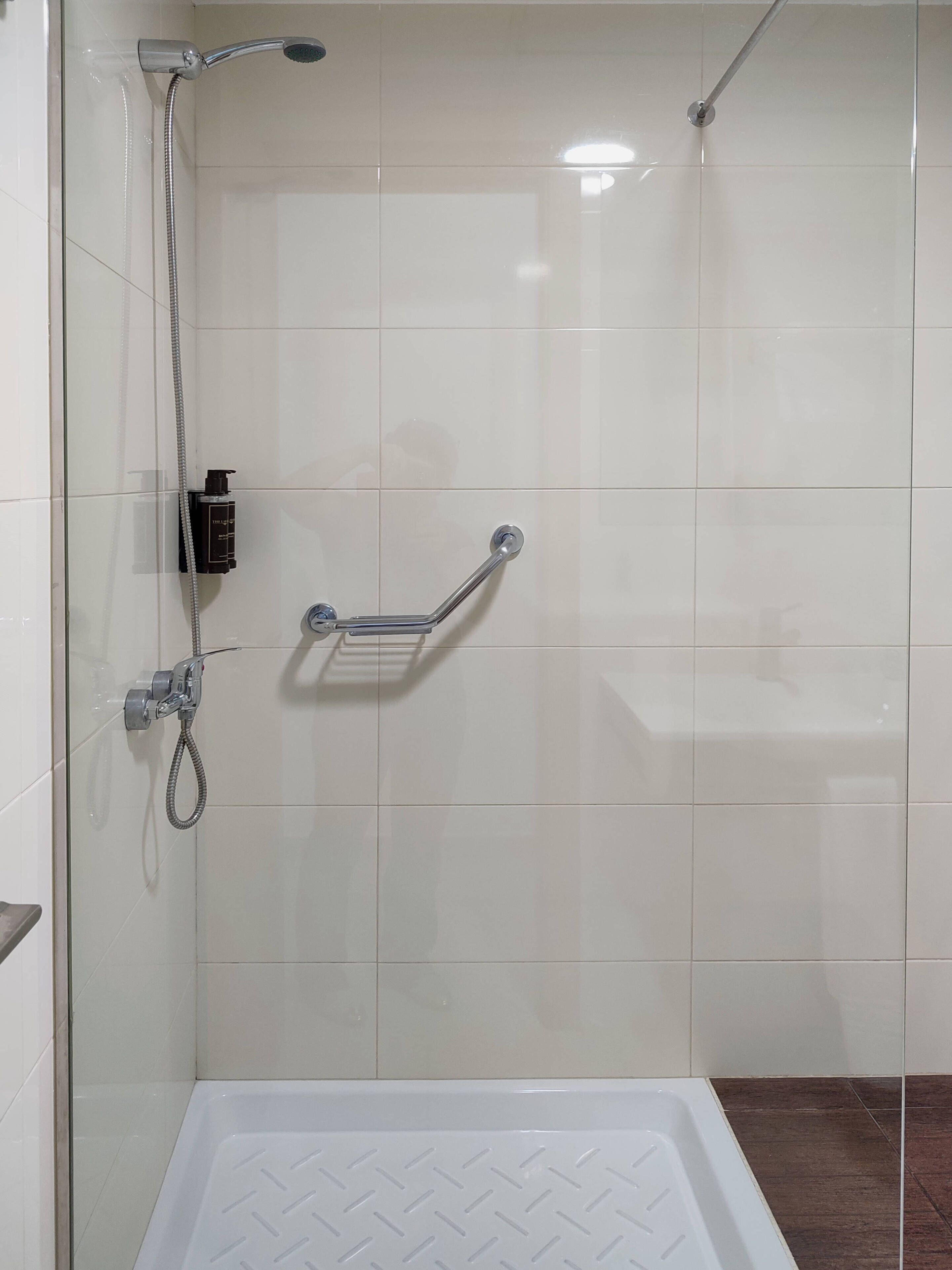 A shower area with a glass door, a handheld showerhead, a handheld shower attachment, and a grab bar.