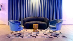 A modern living room with a dark sofa, two blue armchairs, a geometric patterned rug, and a large window with blue curtains. - Hotel Porto (Gandia)