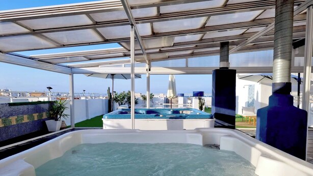 A rooftop pool area with a hot tub and a view of the city skyline. - Hotel Porto (Gandia)