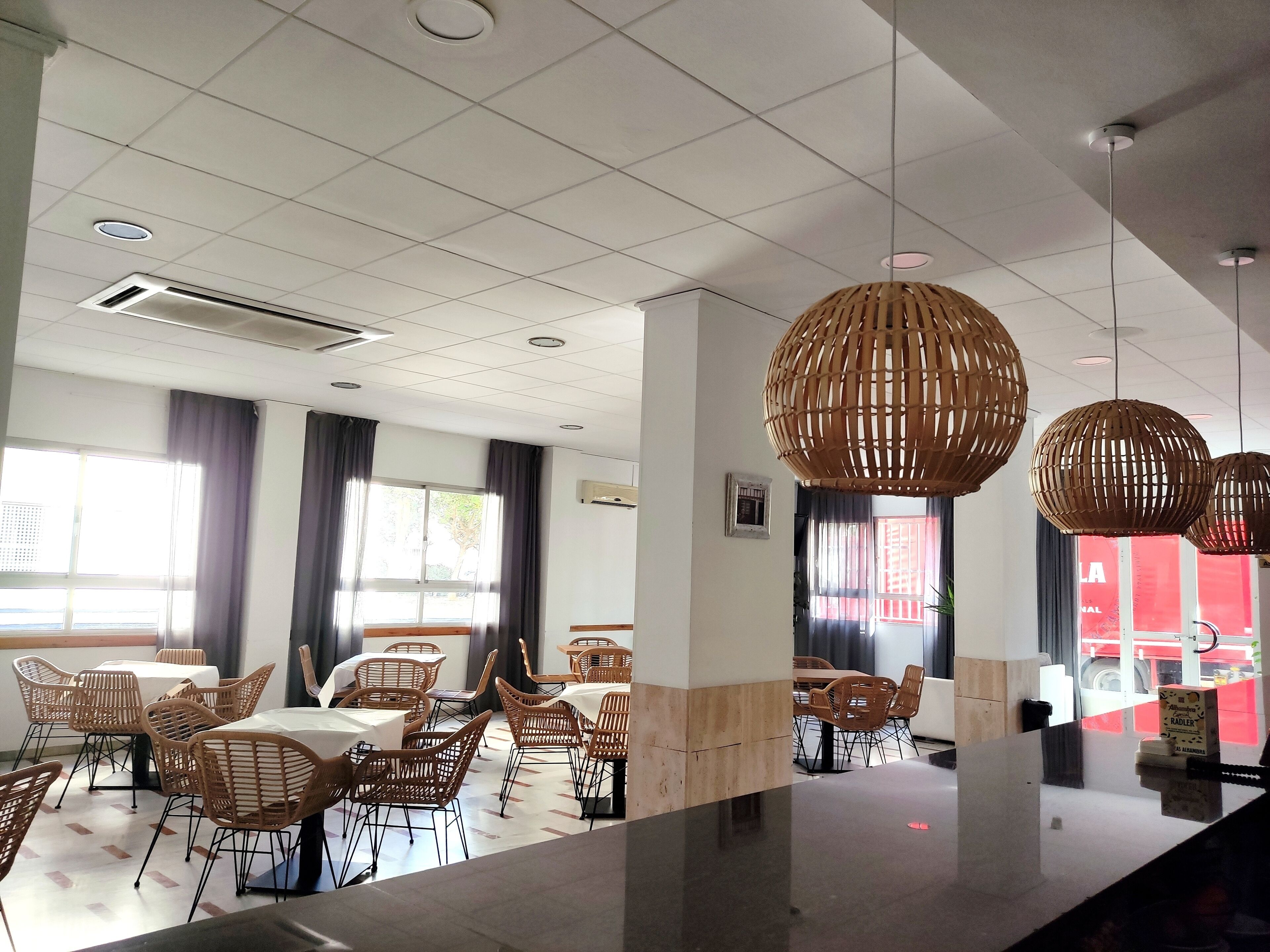 Un restaurant moderne avec des chaises en osier, des tables blanches et des luminaires suspendus en bois.