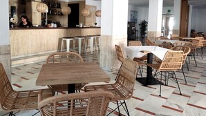 A modern restaurant interior with a bar area, wicker furniture, and a patterned floor. - Hotel Porto (Gandia)