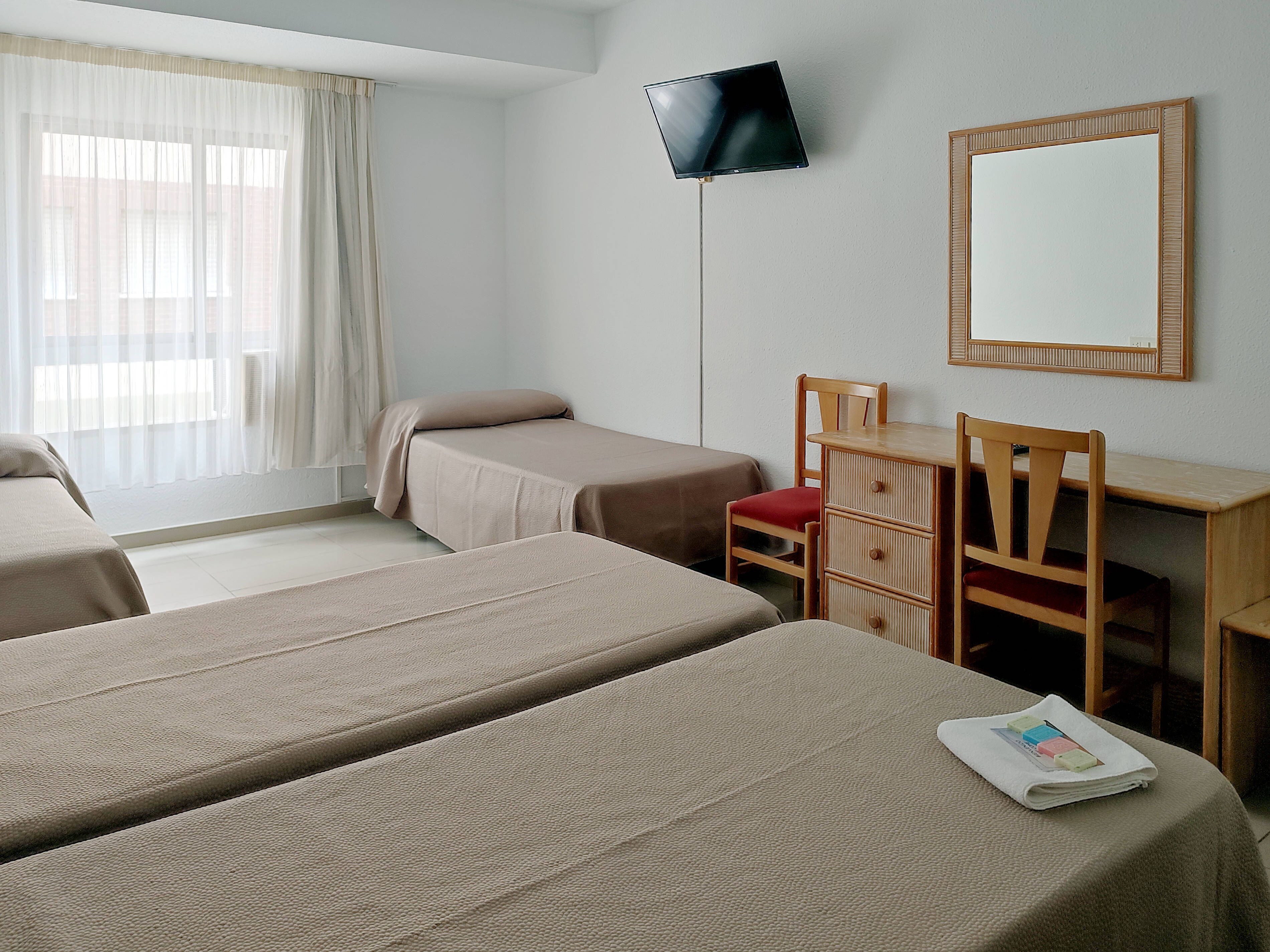 A hotel room with two single beds, a desk with a chair, a television mounted on the wall, and a large mirror.