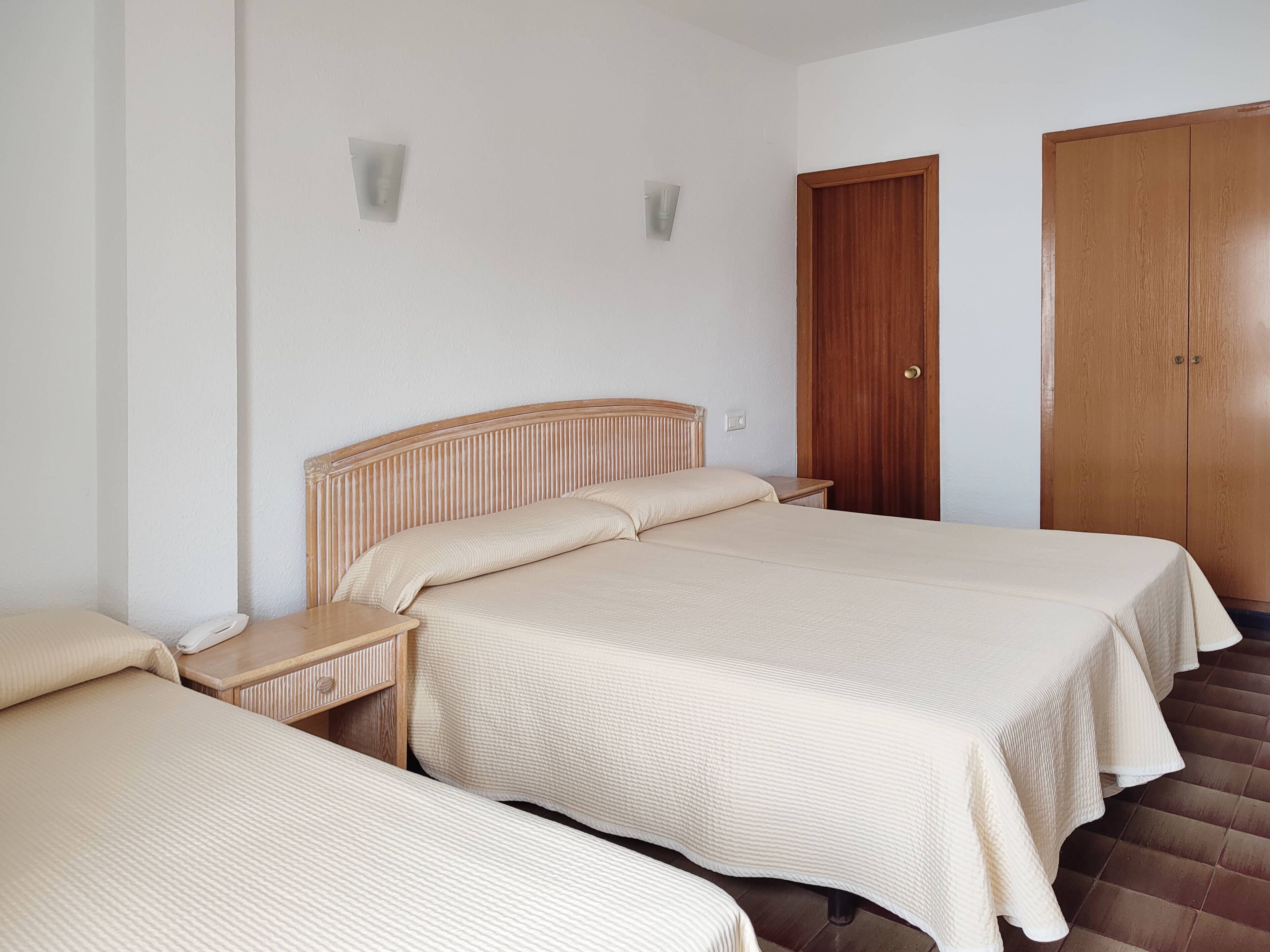 Una habitación de hotel con dos camas, un cabecero de madera, un armario de madera y una mesita de noche con lámpara.