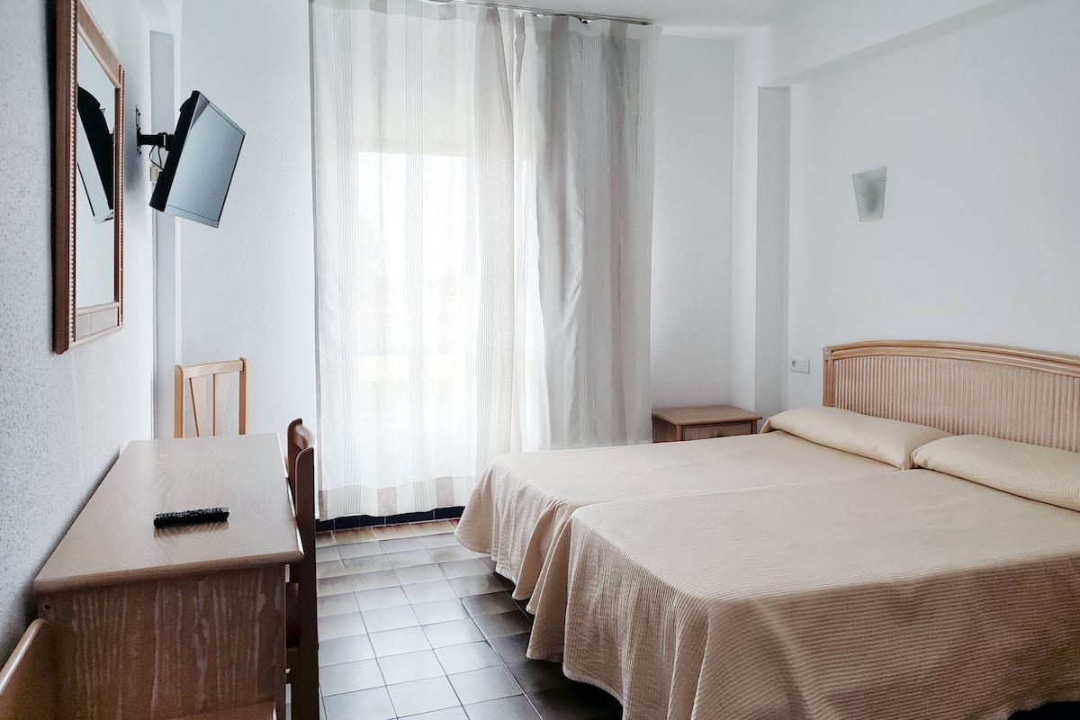 Quarto de hotel com cama, escrivaninha, cadeira, TV fixada na parede e janela com cortinas.