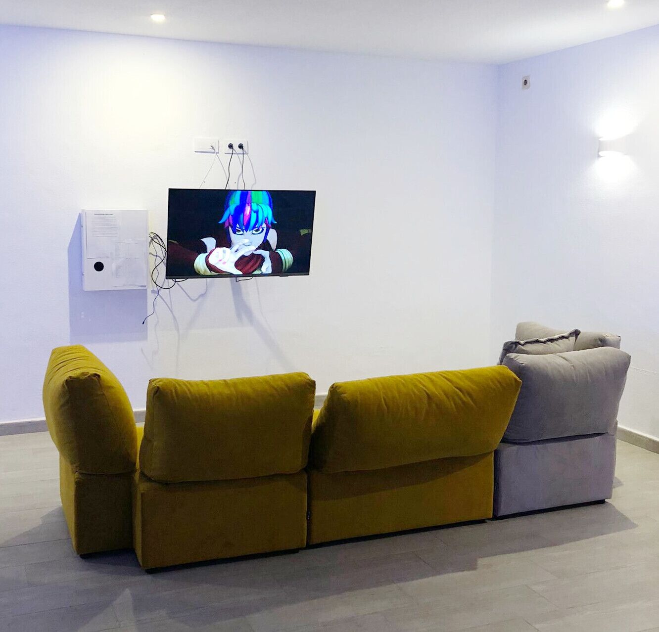 Una sala de estar moderna con un televisor de pantalla plana montado en la pared, un sofá y un sillón pequeño.