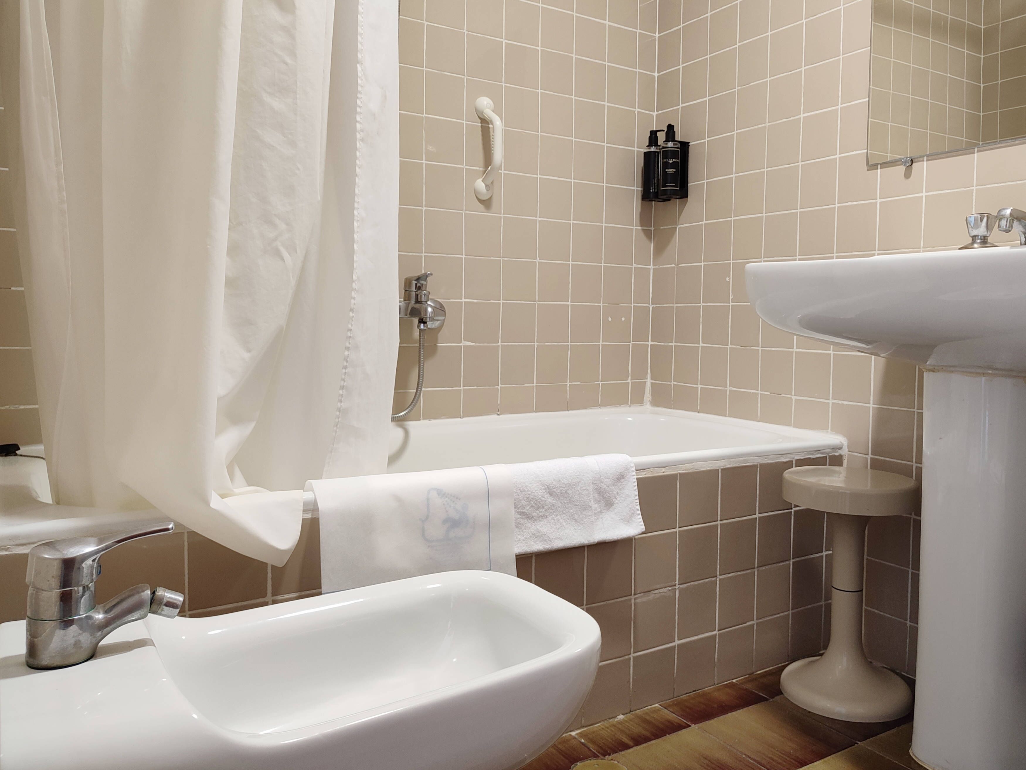 A bathroom with a bathtub, a sink, and a bidet. There is a shower curtain, a towel, and a soap dispenser on the wall.