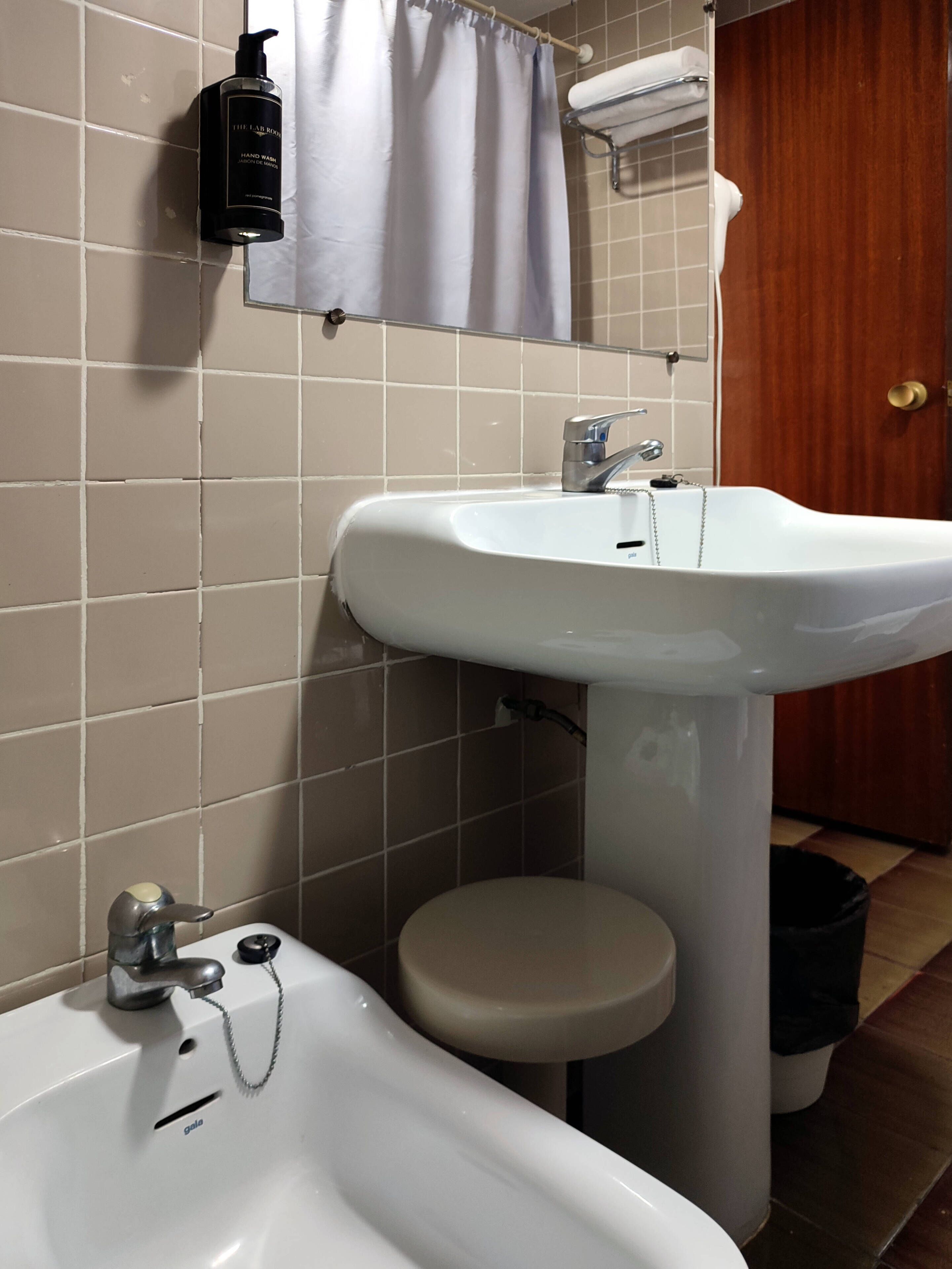 Une salle de bain avec un lavabo blanc, un miroir, un porte-serviettes et un rideau de douche.