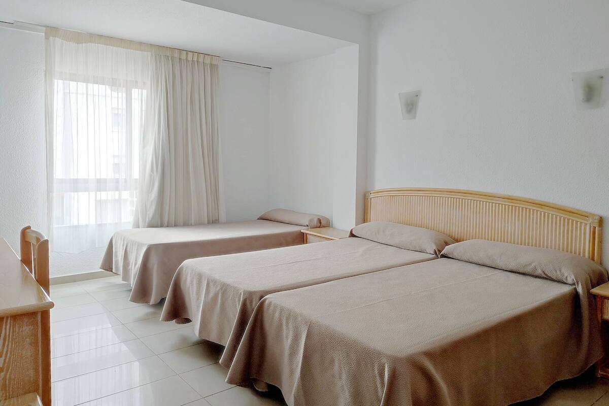 Quarto de hotel com duas camas de solteiro, uma escrivaninha e uma cadeira.