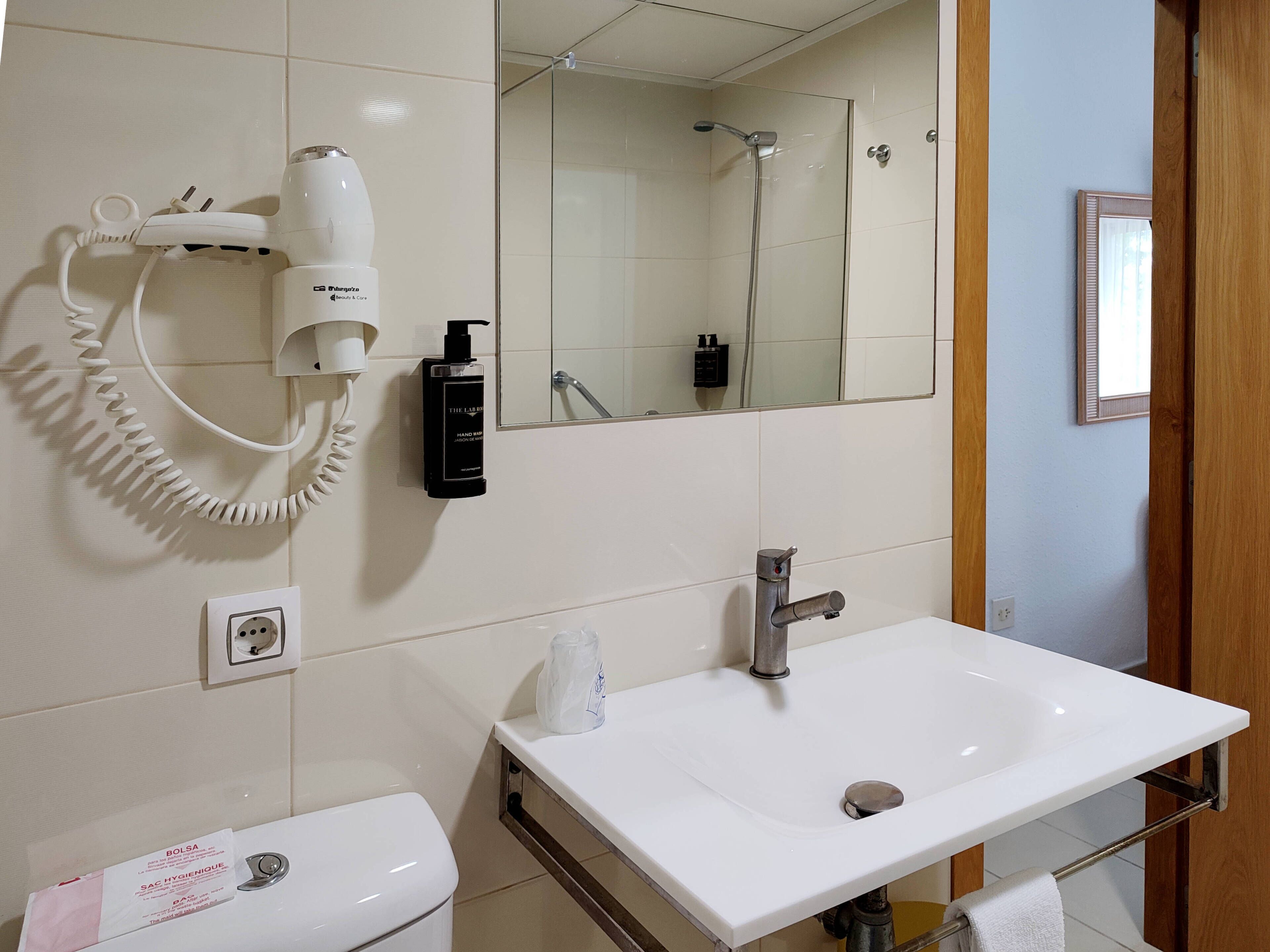 A bathroom with a white sink, a mirror, a hairdryer, and a towel rack.