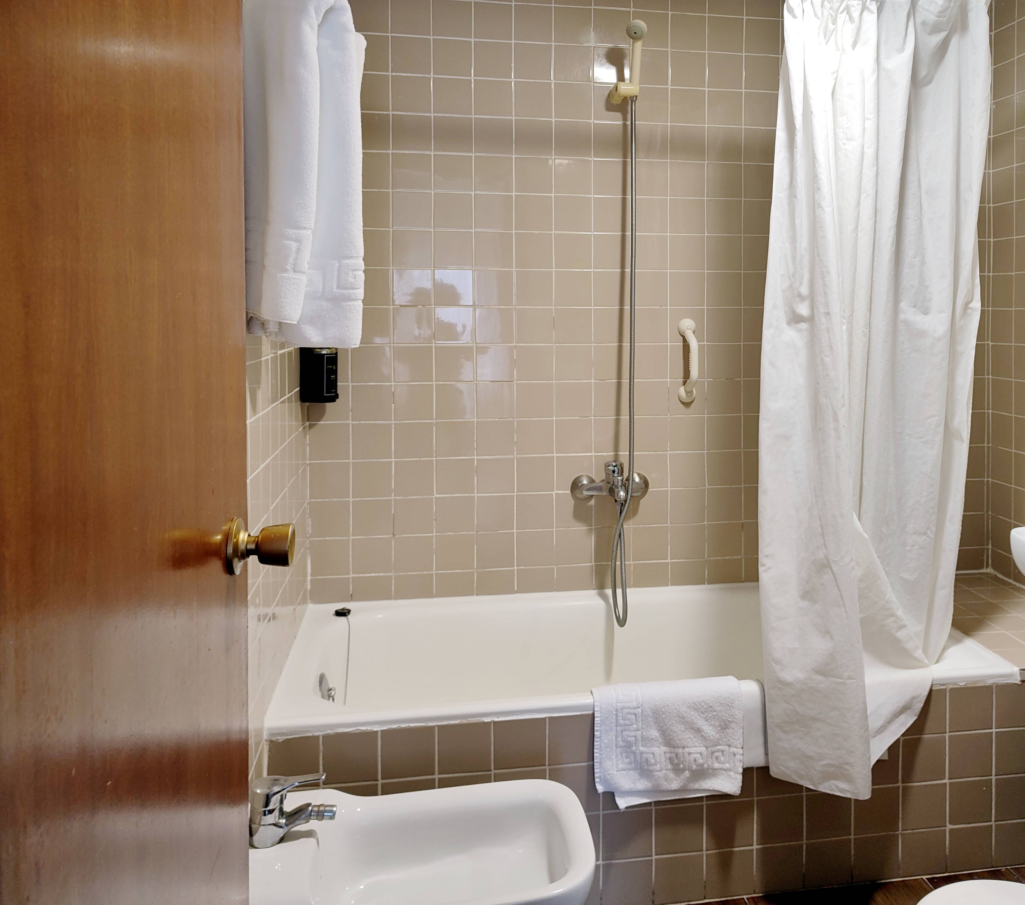 A bathroom with a bathtub, a shower, and a toilet. There are towels hanging on the wall and a door with a brass handle.