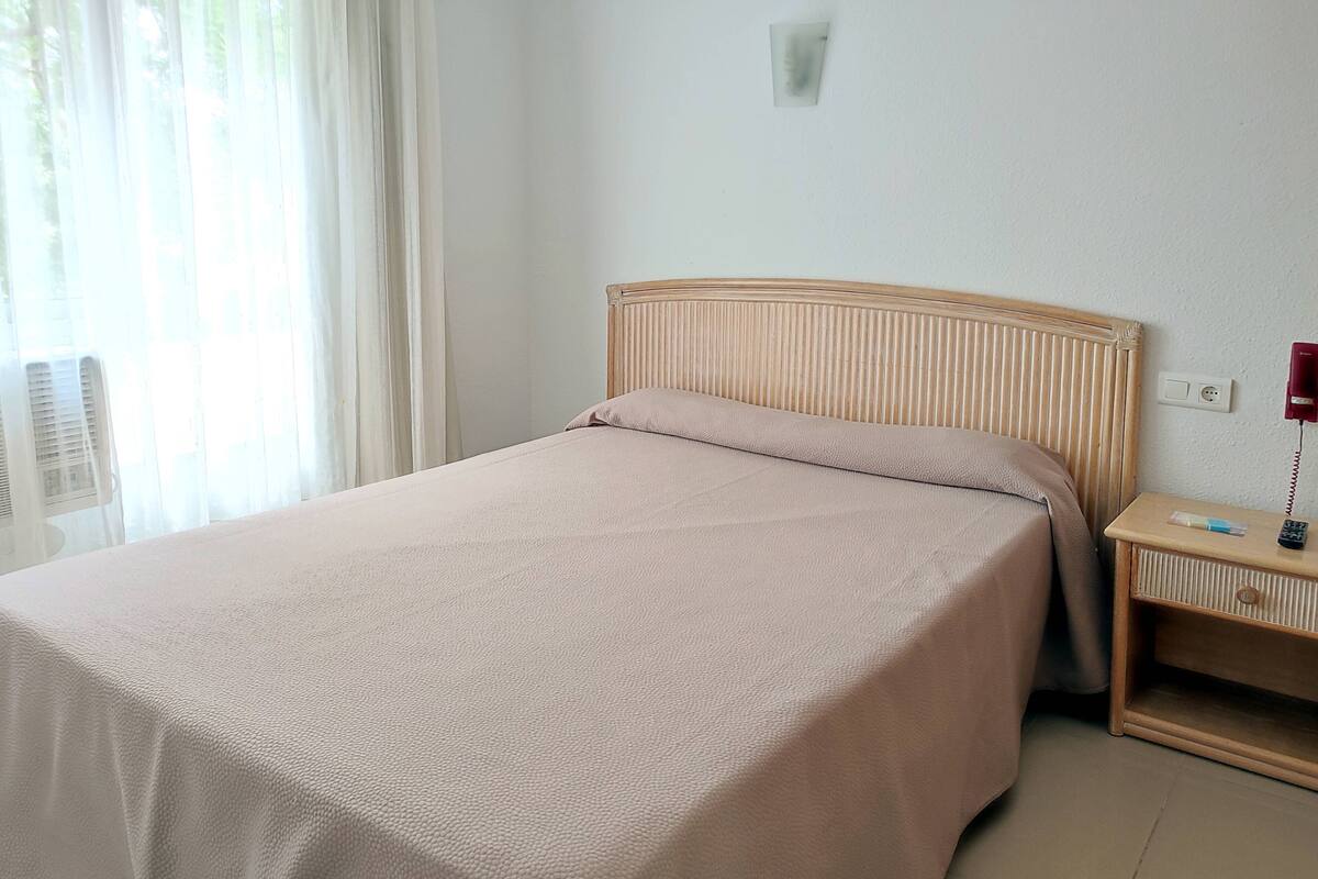Uma cama bem arrumada com cabeceira de madeira, mesa de cabeceira com abajur e telefone.