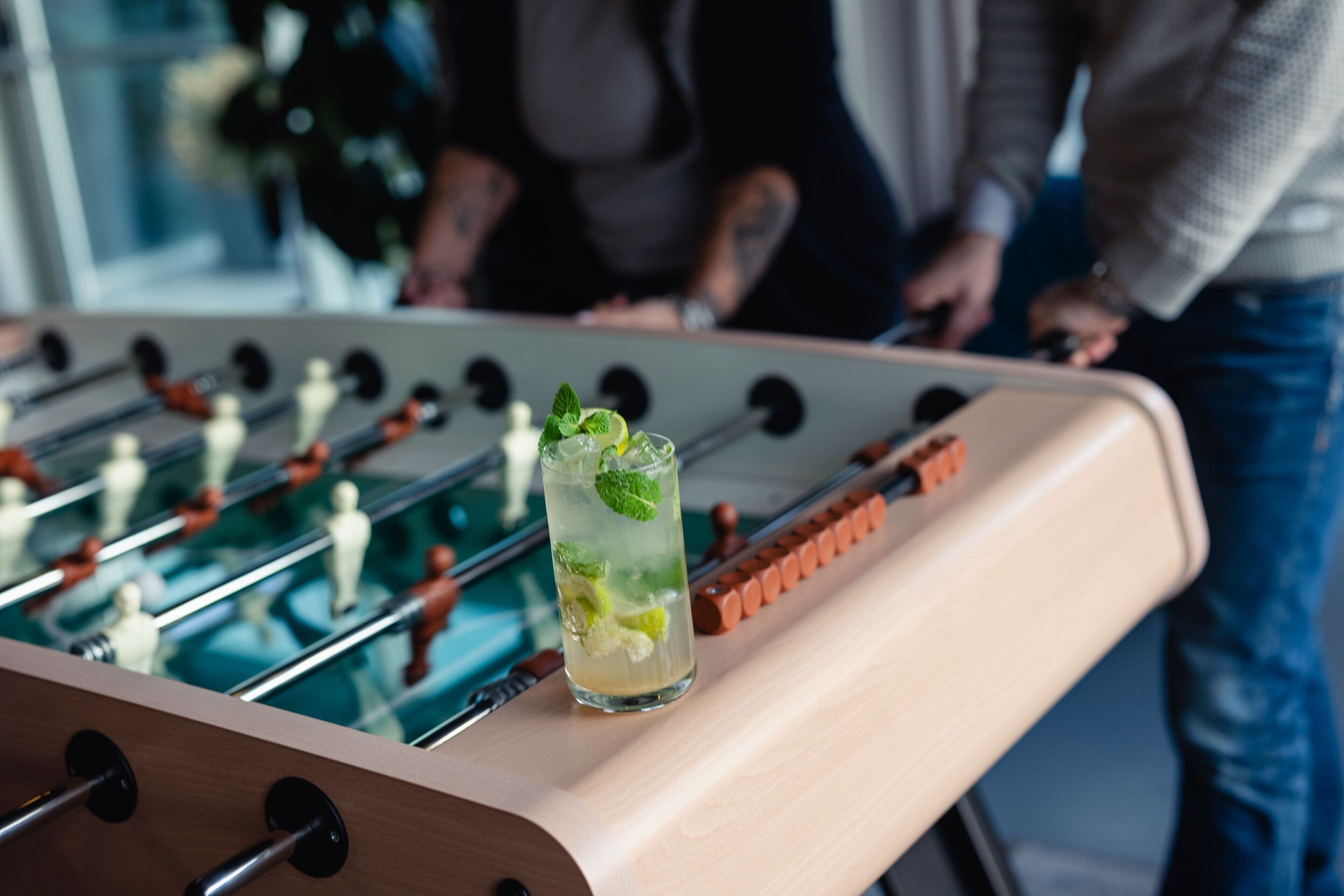 A foosball table with a glass of a beverage containing mint leaves.