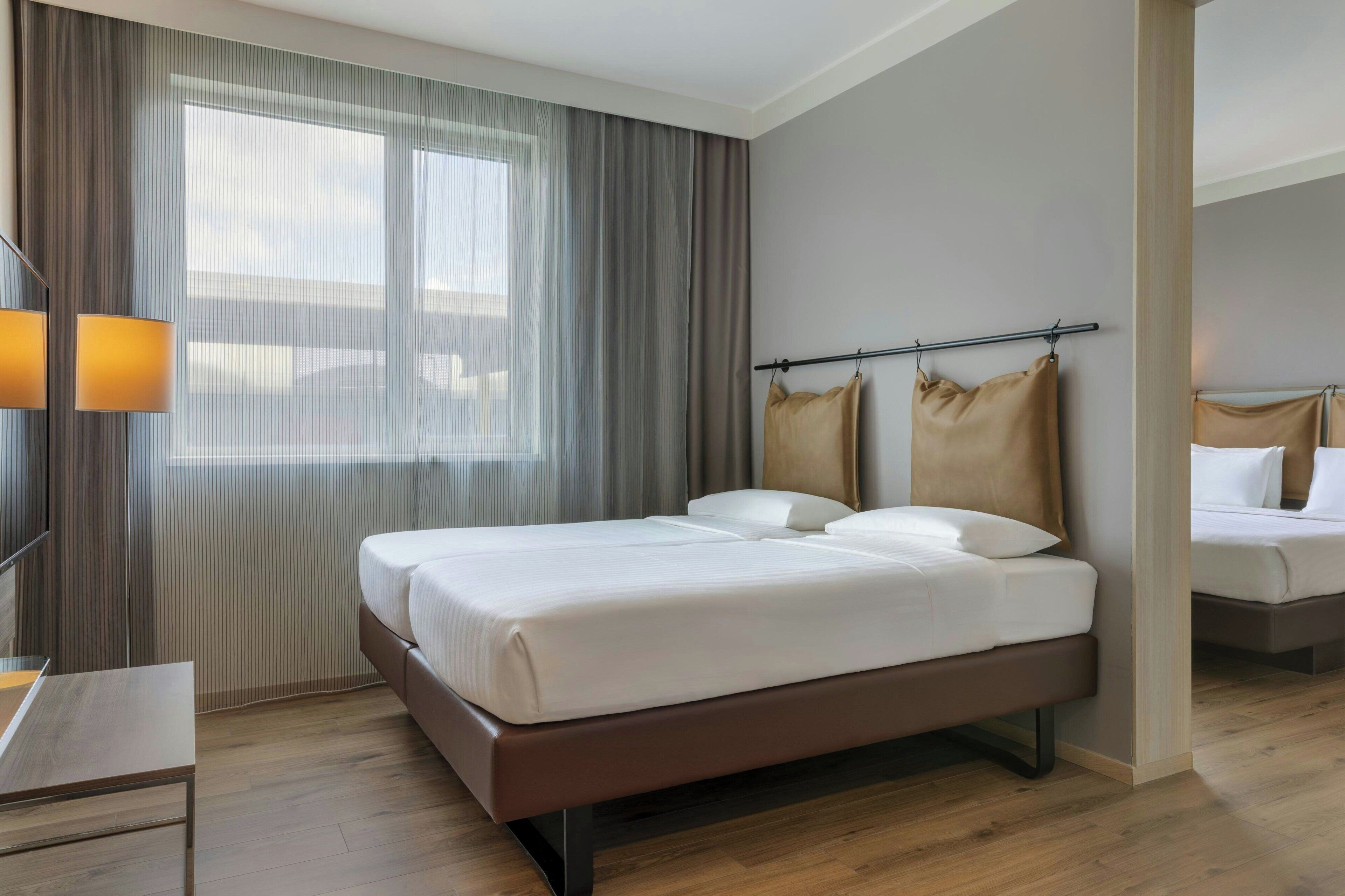 A modern hotel room with a large bed, a bedside table, and a window with curtains.