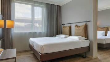 A modern hotel room with a large bed, a bedside table, and a window with curtains.