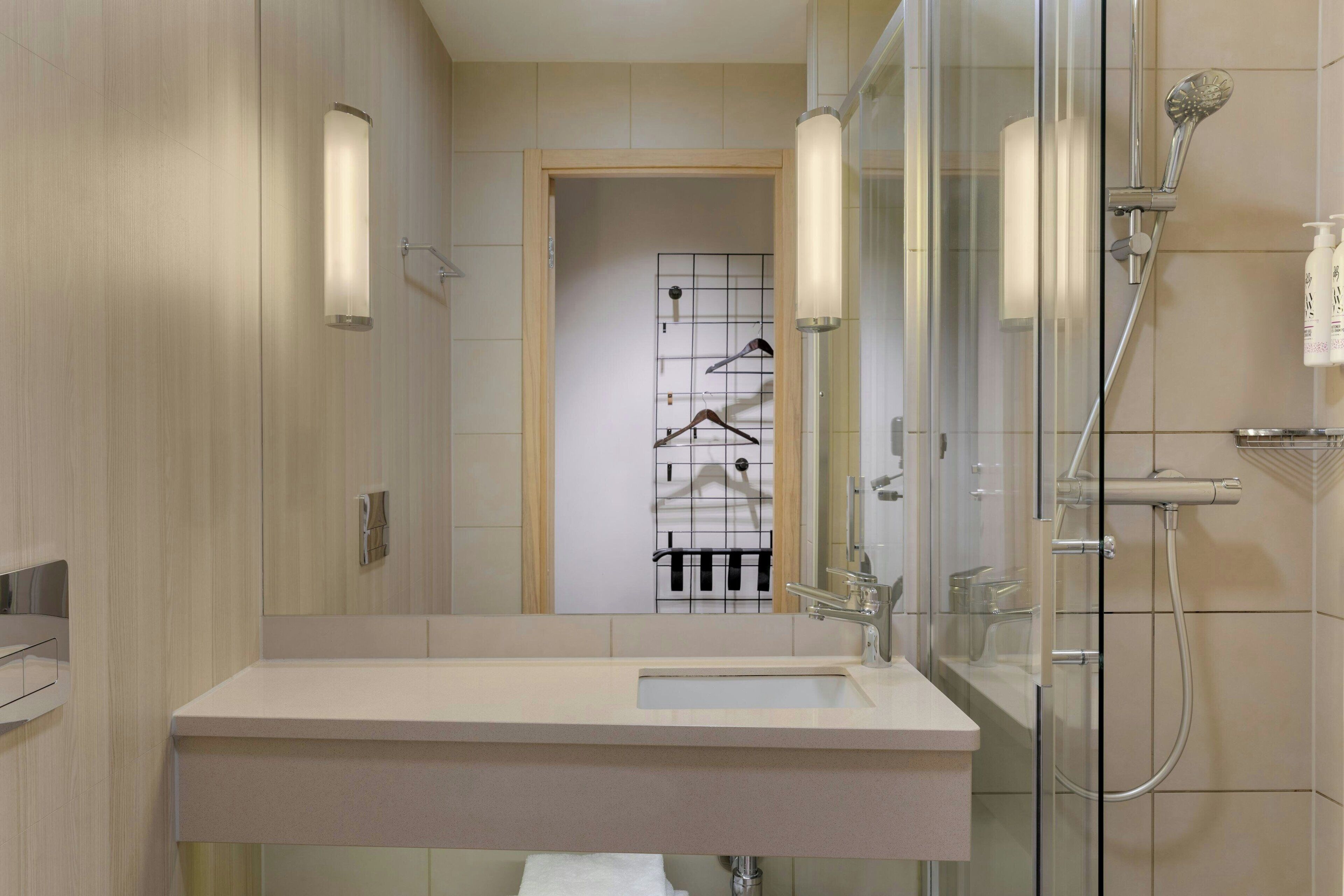 Un bagno moderno con box doccia in vetro, un lavabo con specchio e un portasacchiuili in secondo piano.