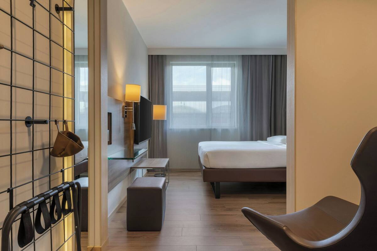 A hotel room with a bed, a TV, a desk, a chair, and a window with curtains.