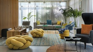 A modern living room with a sofa, armchairs, and a coffee table. There are potted plants and a large window with sheer curtains.