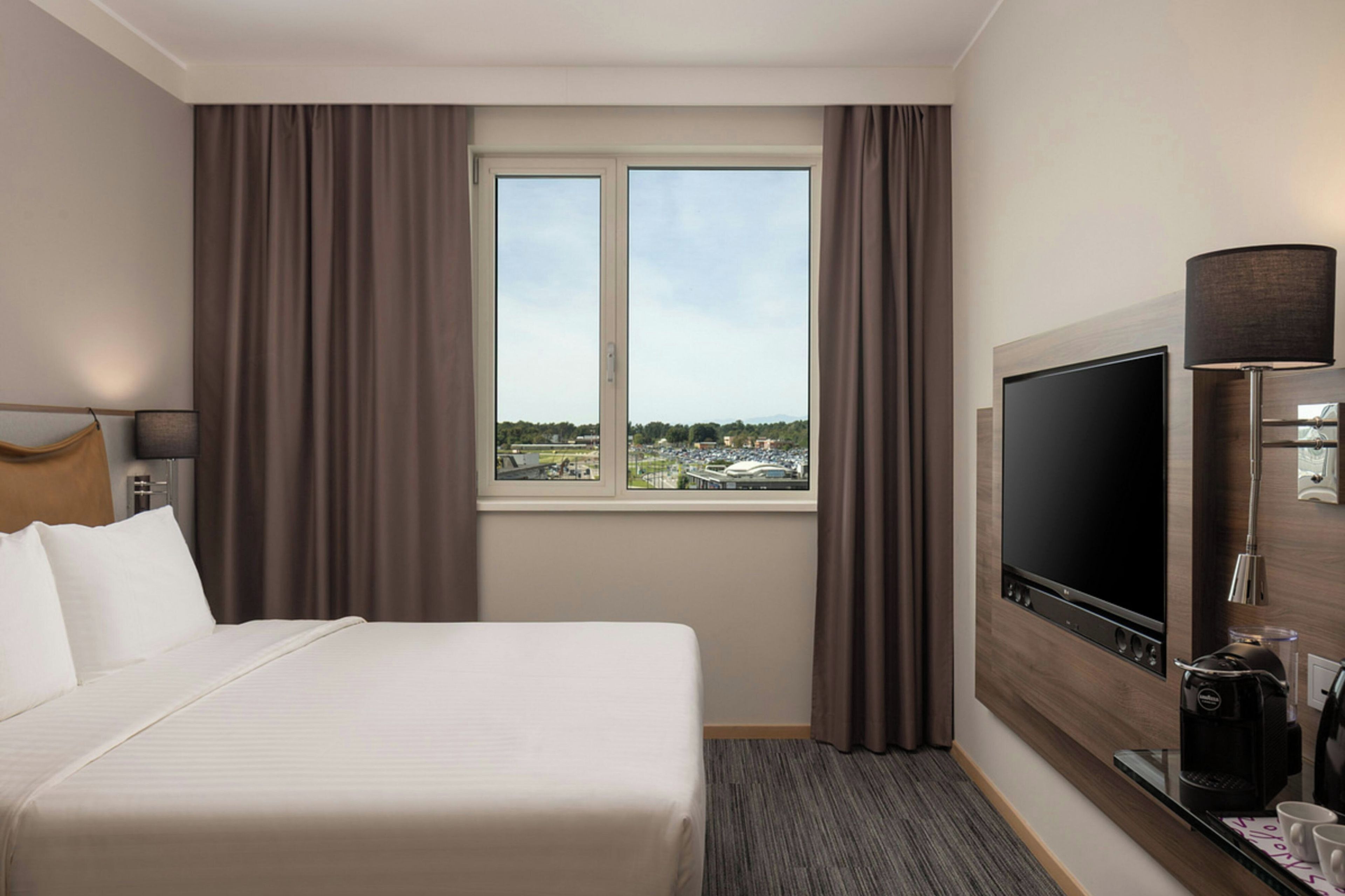 Une chambre d’hôtel avec un lit, une télévision, une machine à café et une vue sur la ville par la fenêtre.