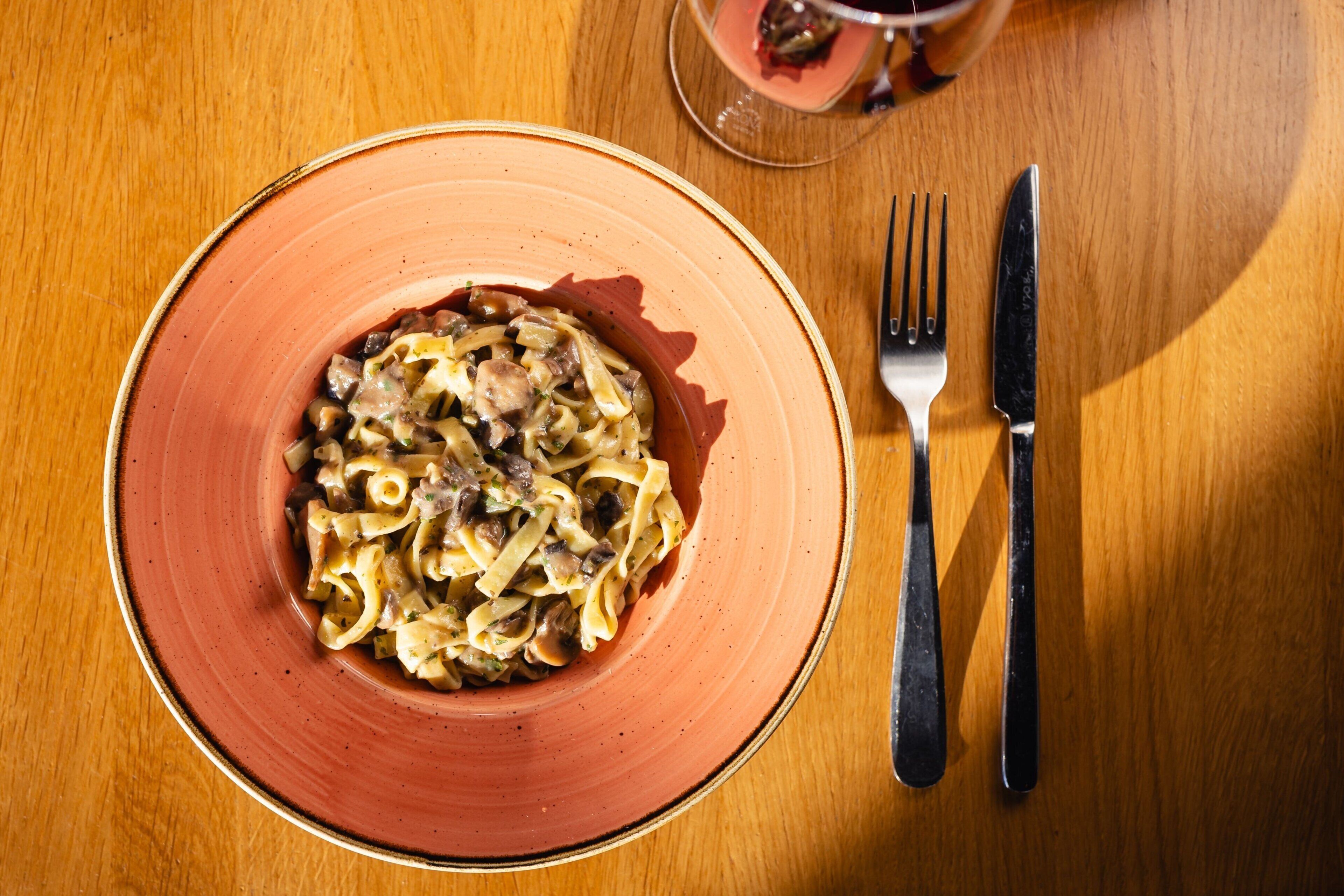Ein Teller Pasta mit cremiger Soße, dazu liegen Messer und Gabel auf einer Holztischplatte.
